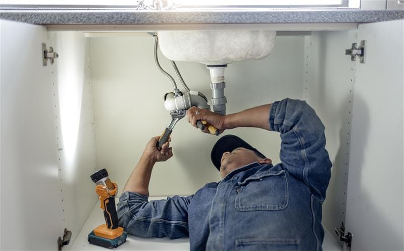 Plumber repairing pipes beneath a bathroom sink in Harrisburg