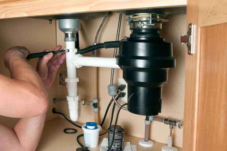 Plumber installing a garbage disposal beneath a kitchen sink in Harrisburg
