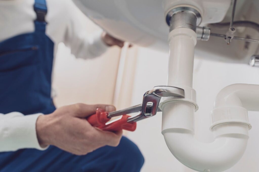 Plumber repairing a white drain pipe beneath a sink in Harrisburg