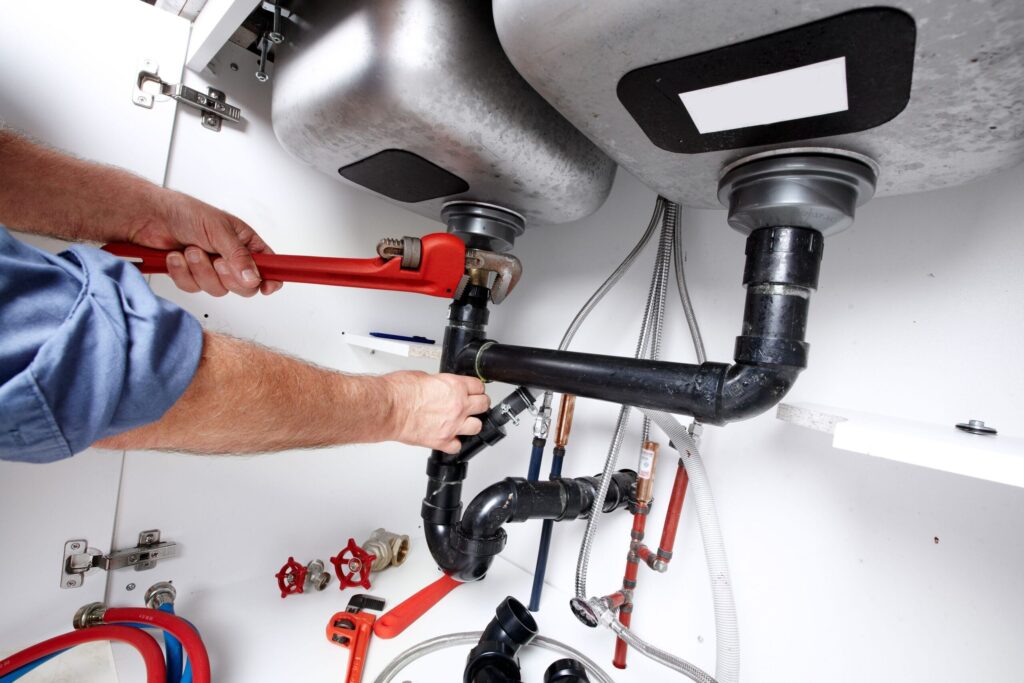 Plumber repairing drain pipes beneath a kitchen sink in Harrisburg